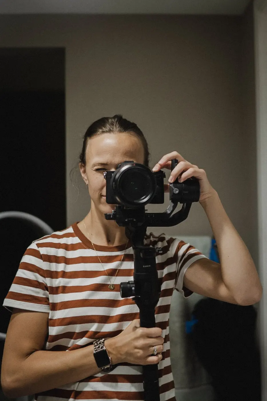 Susan holding her camera on a gimbal, wearing a rust-and-white striped shirt.