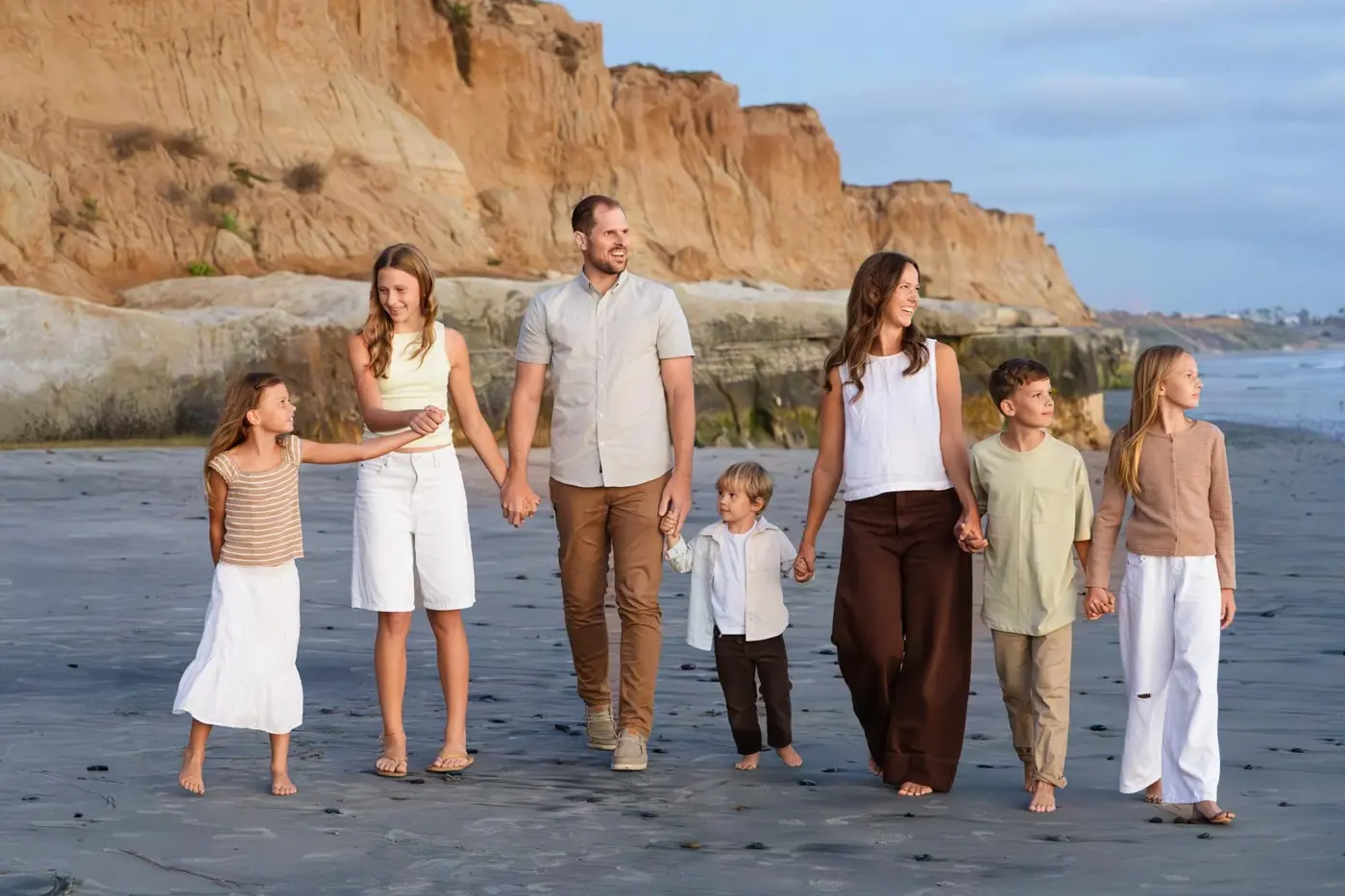 Susan, her husband, and their five children walking together on the beach beside sandstone cliffs.