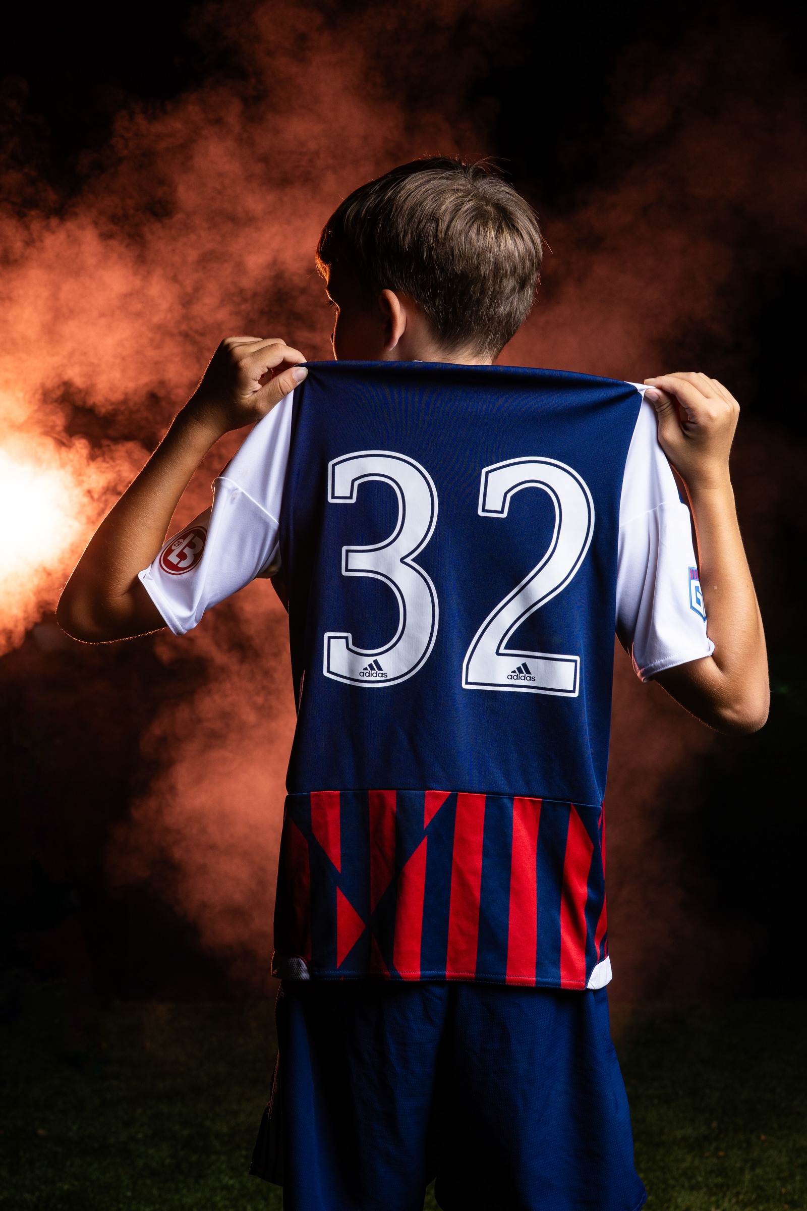 Soccer player faces away from the camera and holds up his jersey showing number 32 against orange smoke.