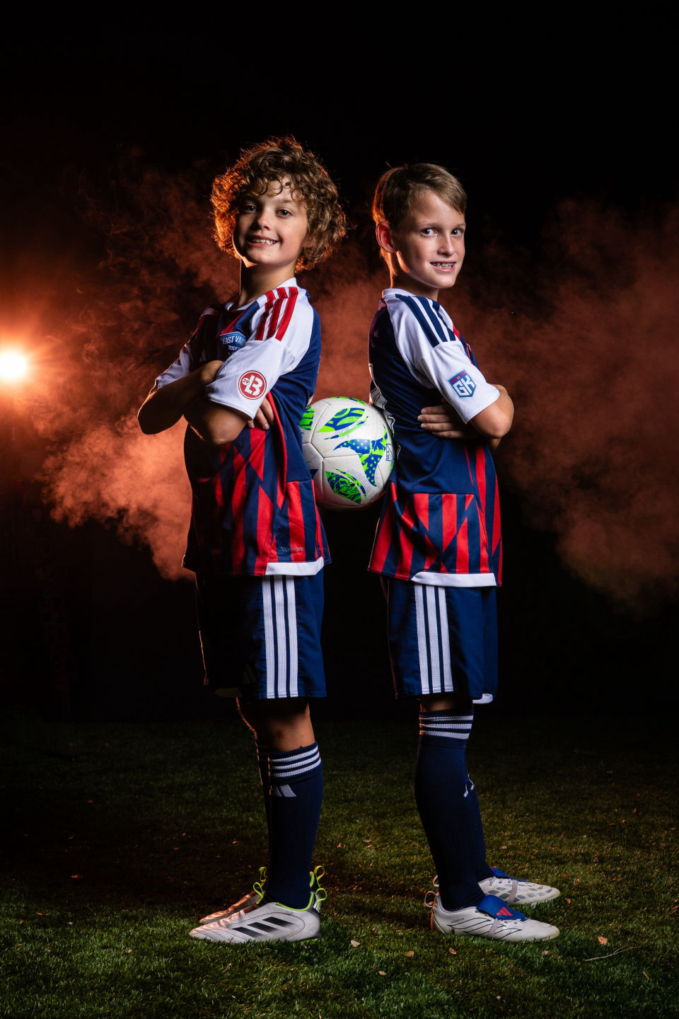 Two smiling soccer teammates pose back to back with their balls.
