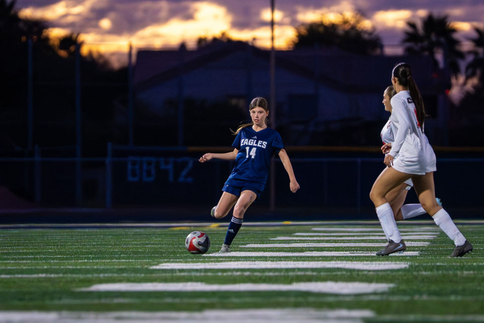 Soccer player winds up for a kick under a colorful twilight sky.