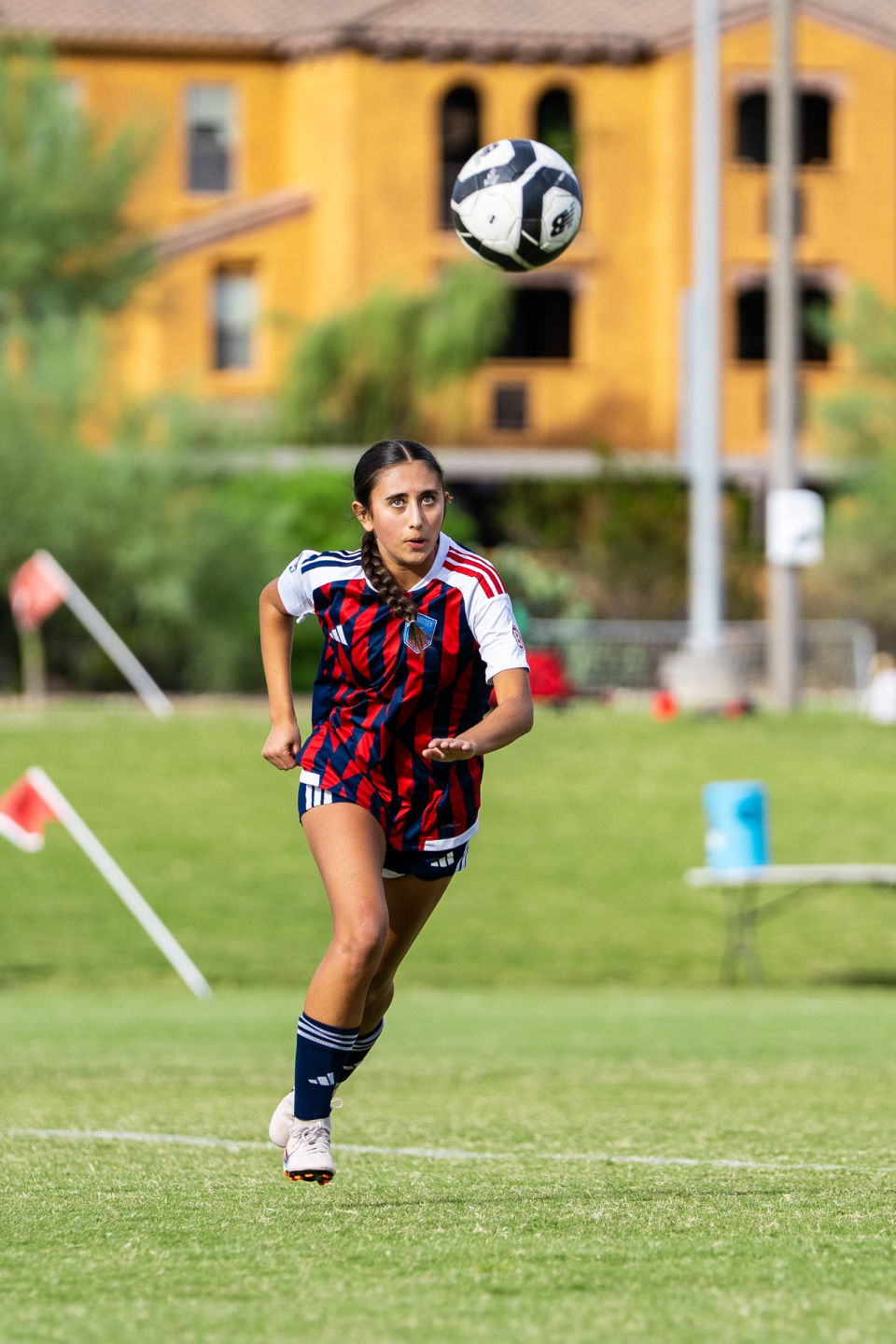 Soccer player in a red and blue striped jersey tracks a ball in the air.