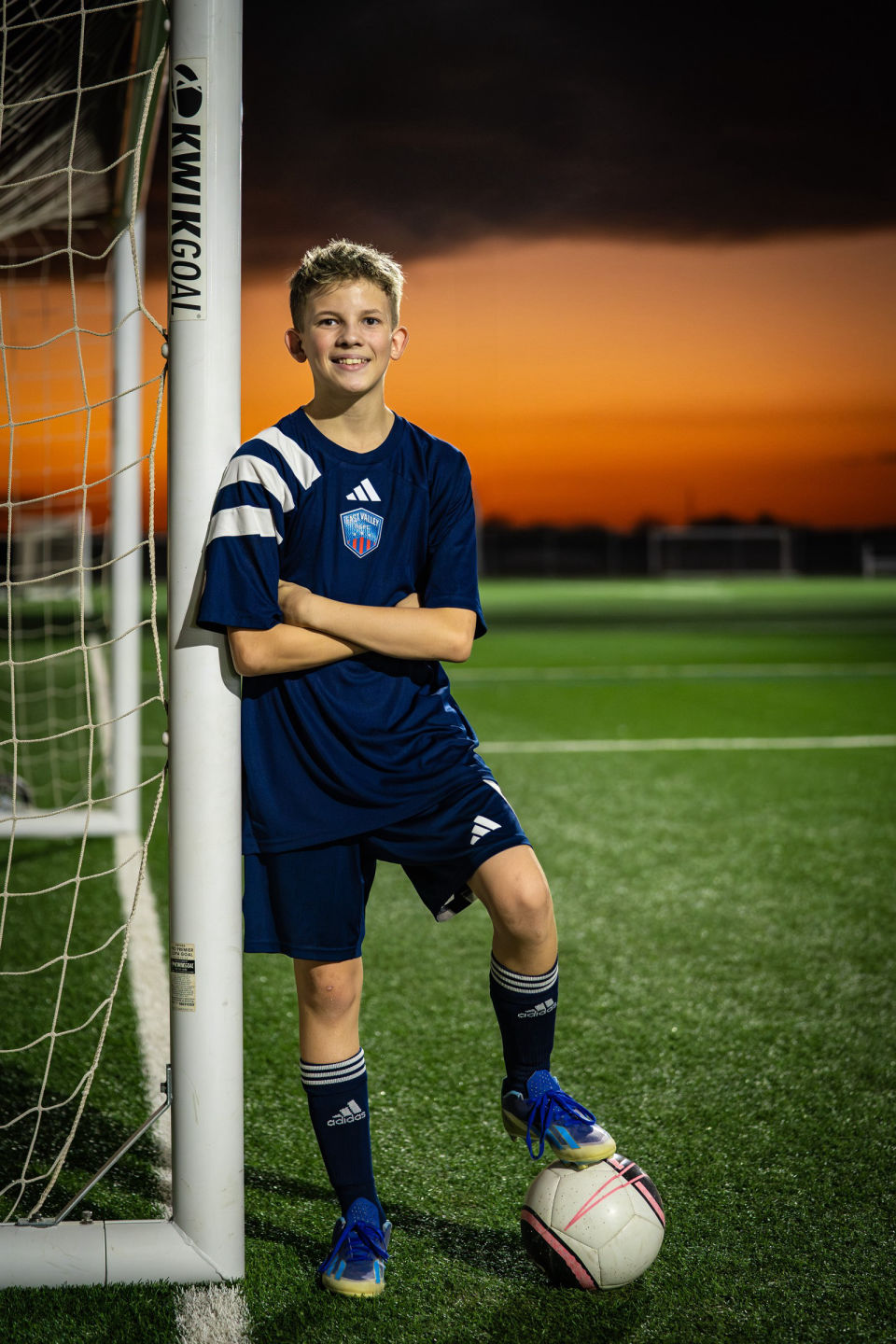Kaysen stands beside the goal with a ball at his foot beneath the sunset.