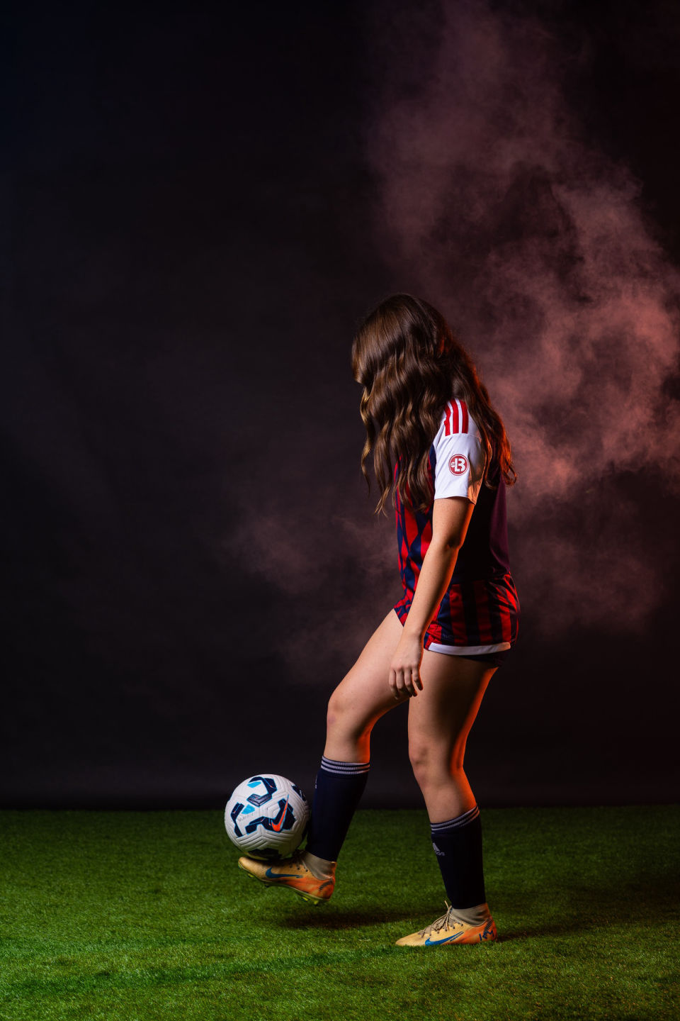 Soccer player balancing a ball on her cleat against a dark smoky backdrop.
