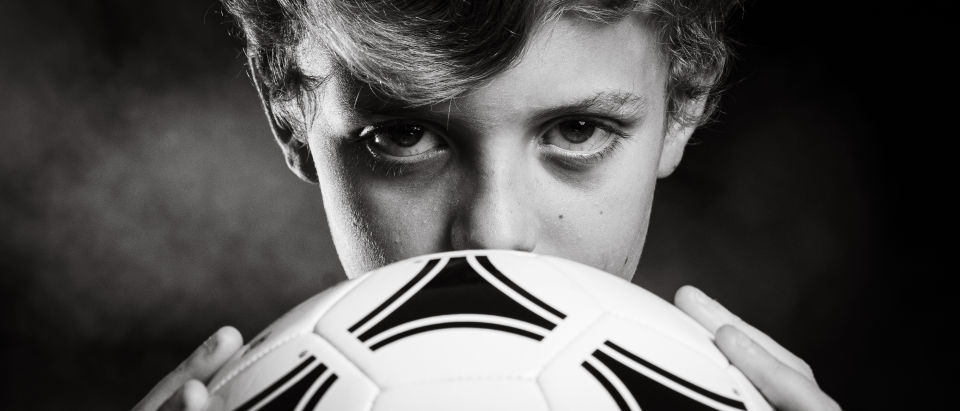 Black and white close portrait of a soccer player looking intently over a soccer ball.