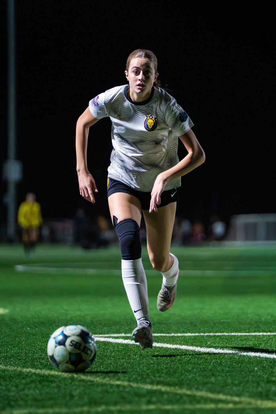 Soccer player in a gray jersey runs toward the ball under stadium lights.