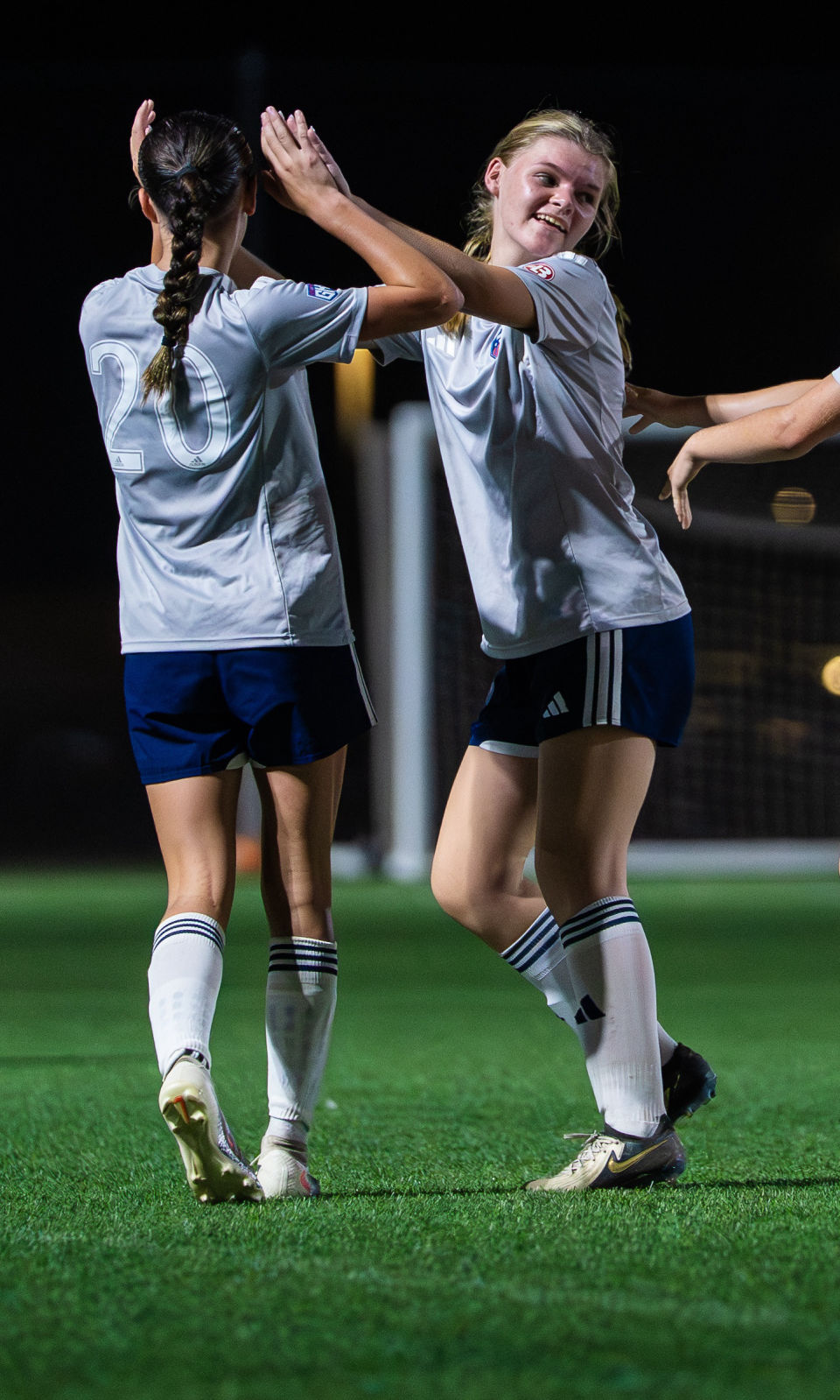 Two soccer teammates share a smiling high-five on the field during a night game.