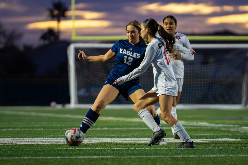 Two soccer players compete for the ball beneath a glowing sunset sky.