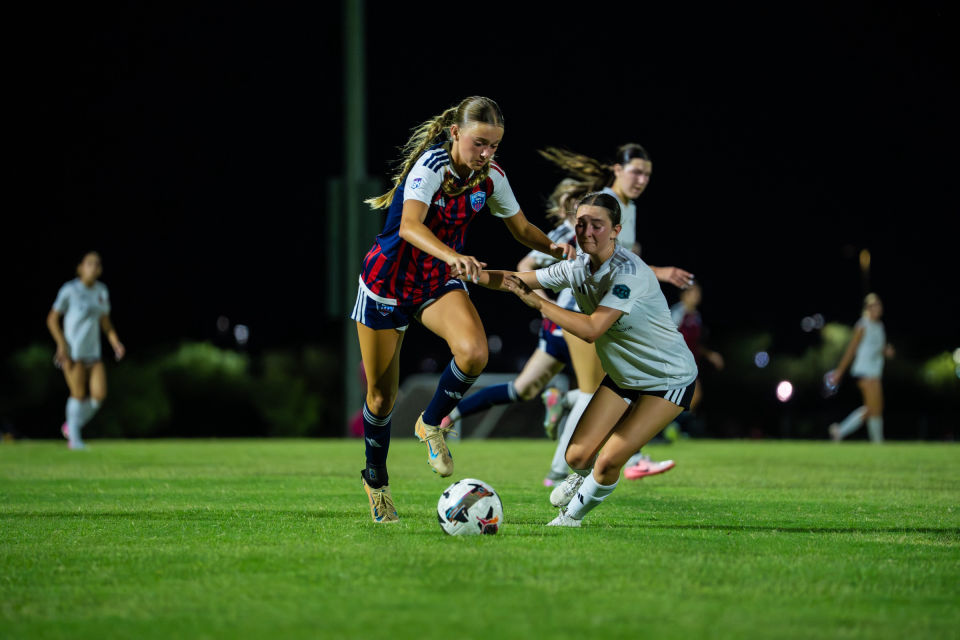 Two soccer players jostle shoulder to shoulder for the ball during a night game.