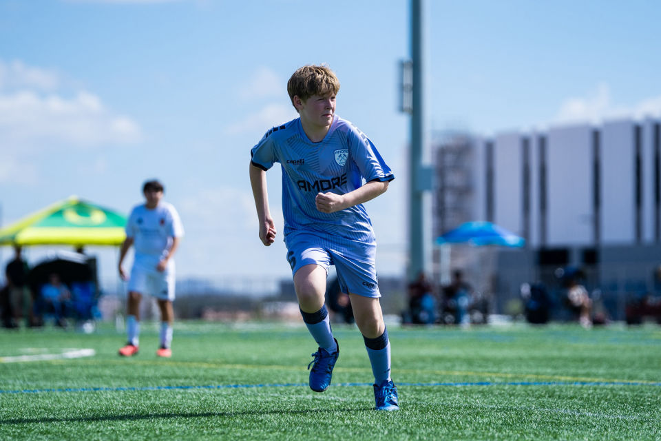 Soccer player in light blue runs forward during a daytime game.