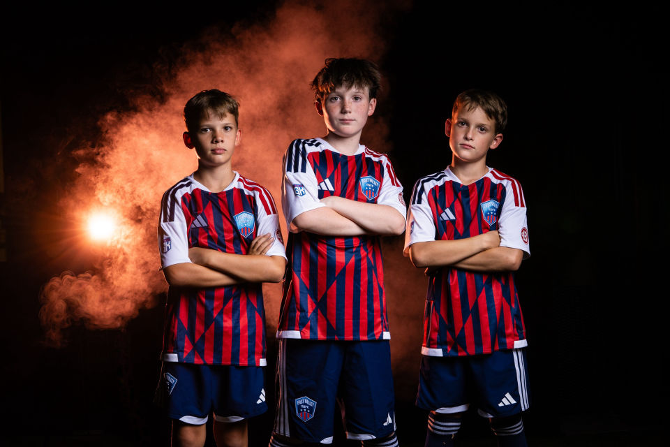 Three soccer teammates pose with folded arms against orange smoke.