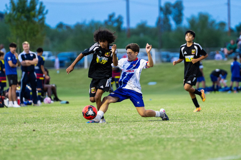 Two soccer players stretch into a close challenge for a red ball.