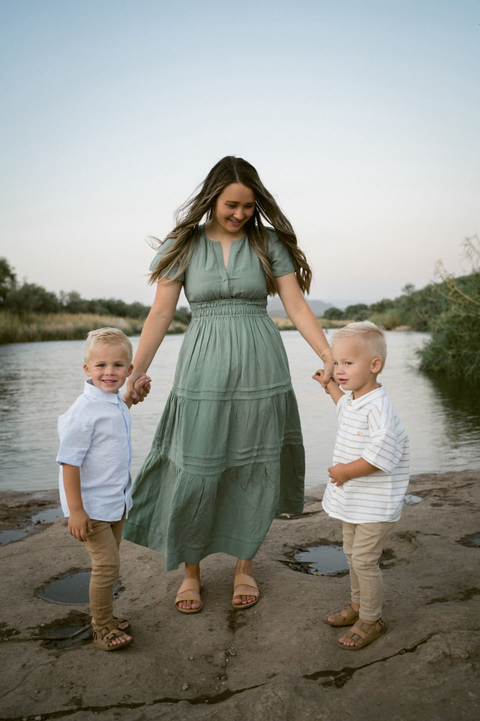 Mother in a green dress walks hand in hand with her two boys by the river.