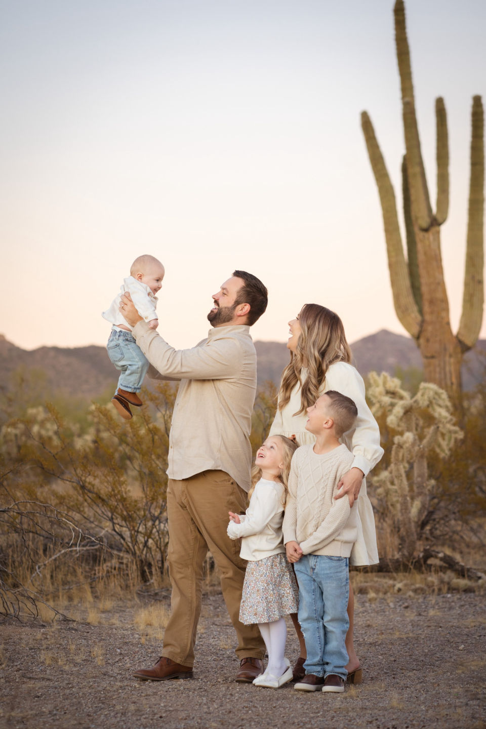 Family watches as a father lifts his smiling baby beneath a saguaro.