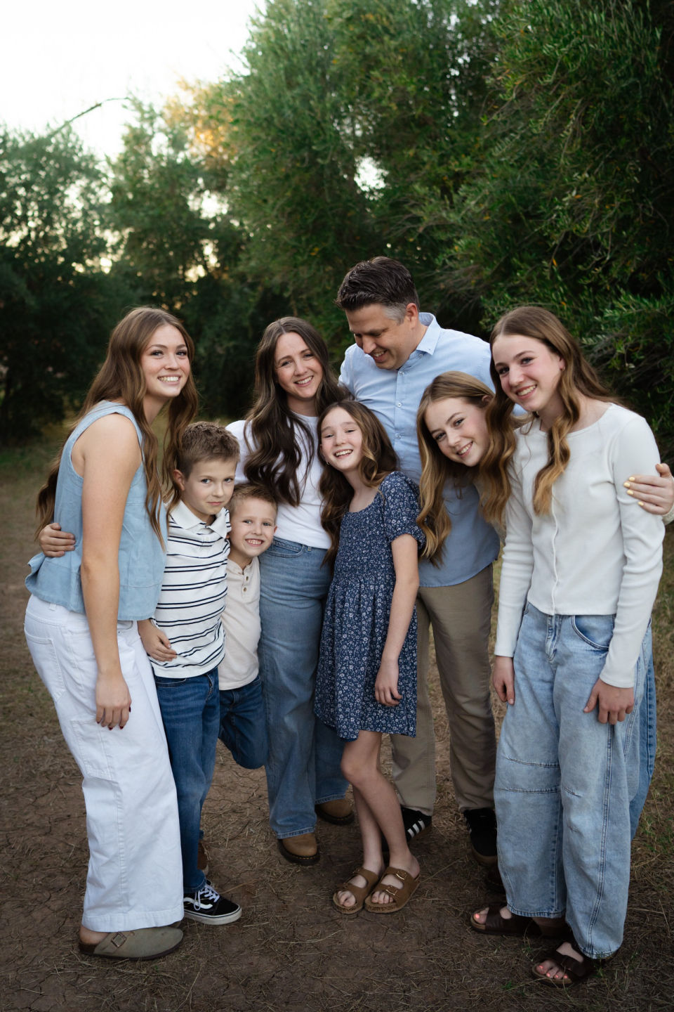 Family smiles and leans together on a shaded path.
