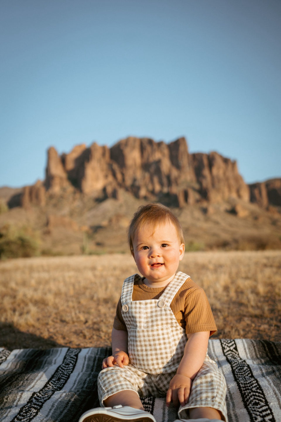 Young child sitting on a blanket in the desert.