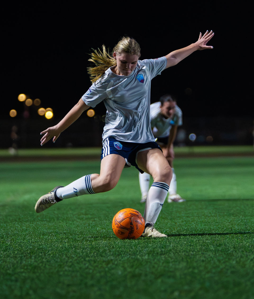 Soccer player winds up to strike an orange ball under the field lights.