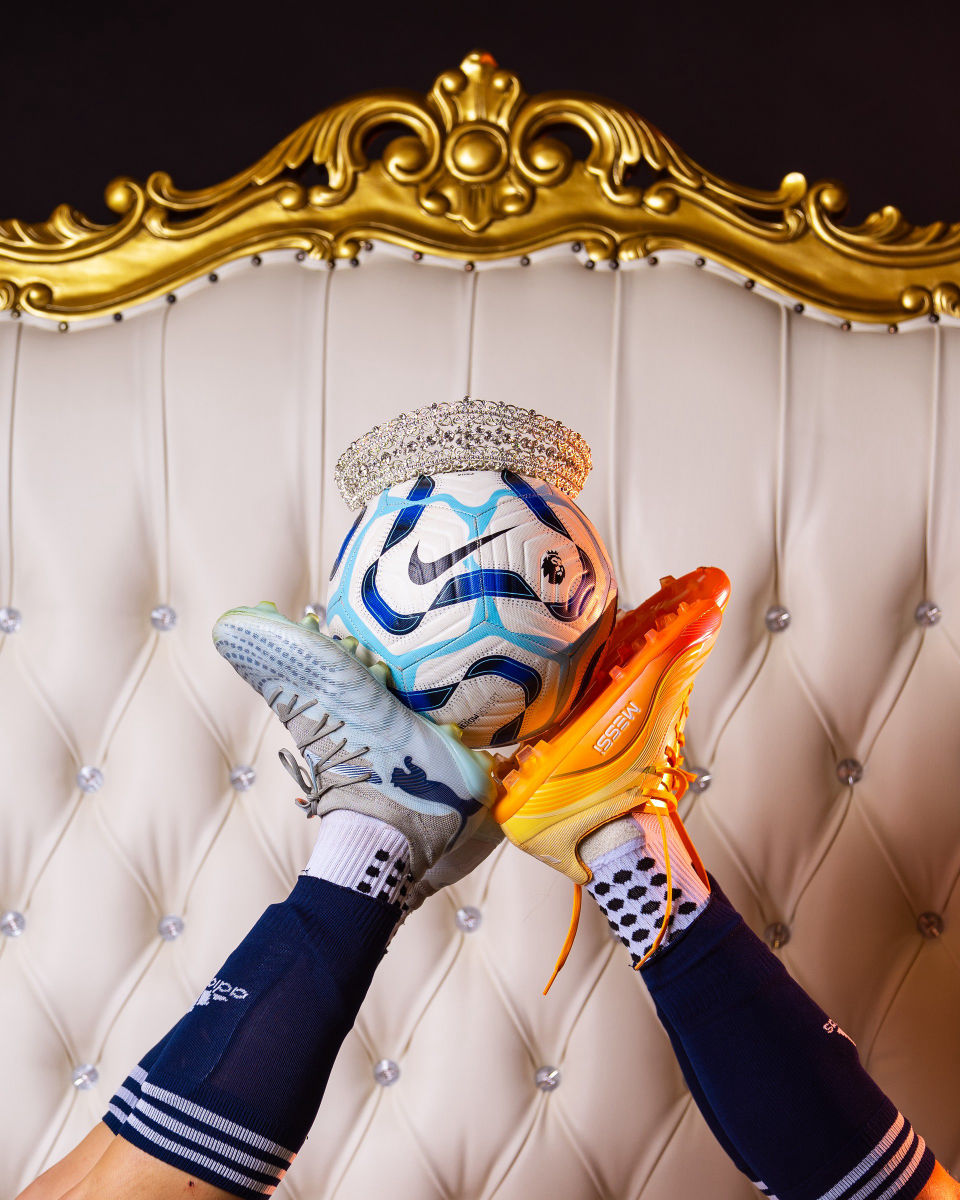 Two raised soccer cleats balance a crowned soccer ball in front of a white and gold throne.