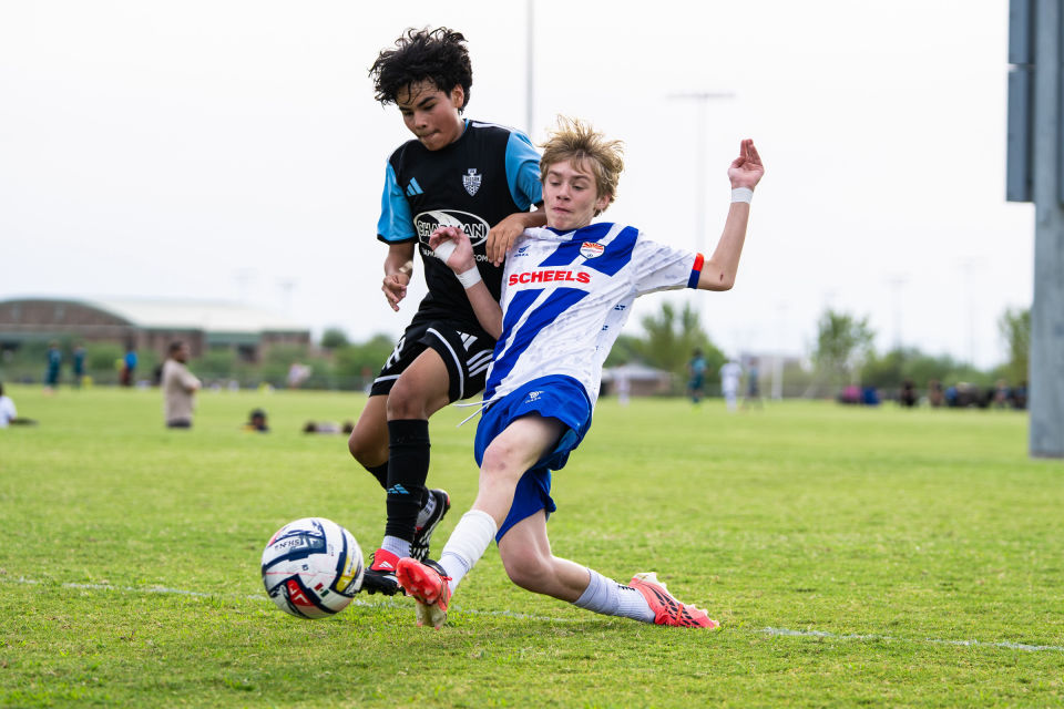 Soccer player in white and blue slides into a tackle as an opponent challenges for the ball.