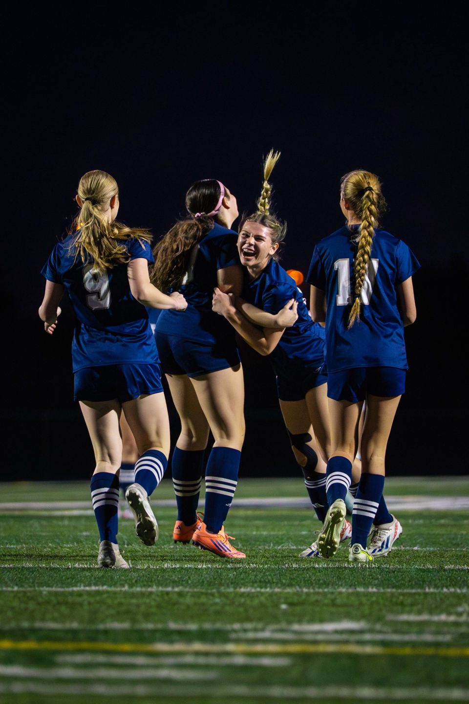 Smiling soccer teammates embrace in celebration during a night game.