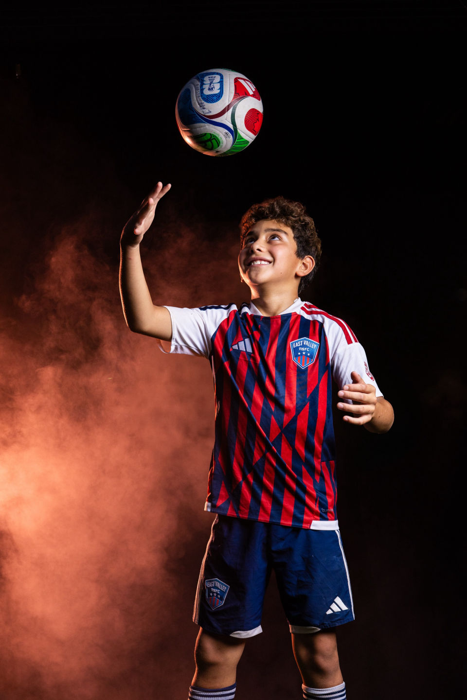 Smiling soccer player tosses a ball in the air.