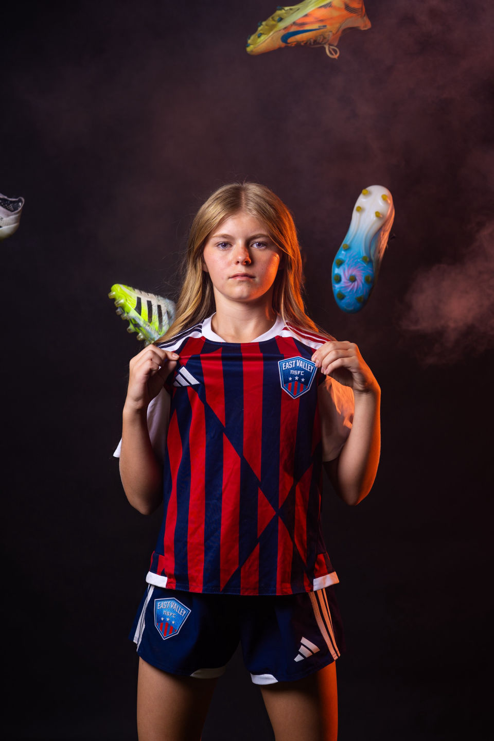 Soccer player holding out her team jersey beneath airborne cleats.