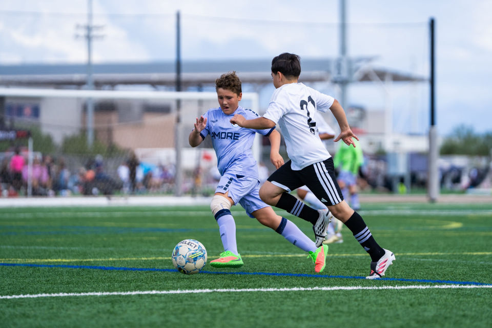 Two soccer players race shoulder to shoulder with the ball at their feet.