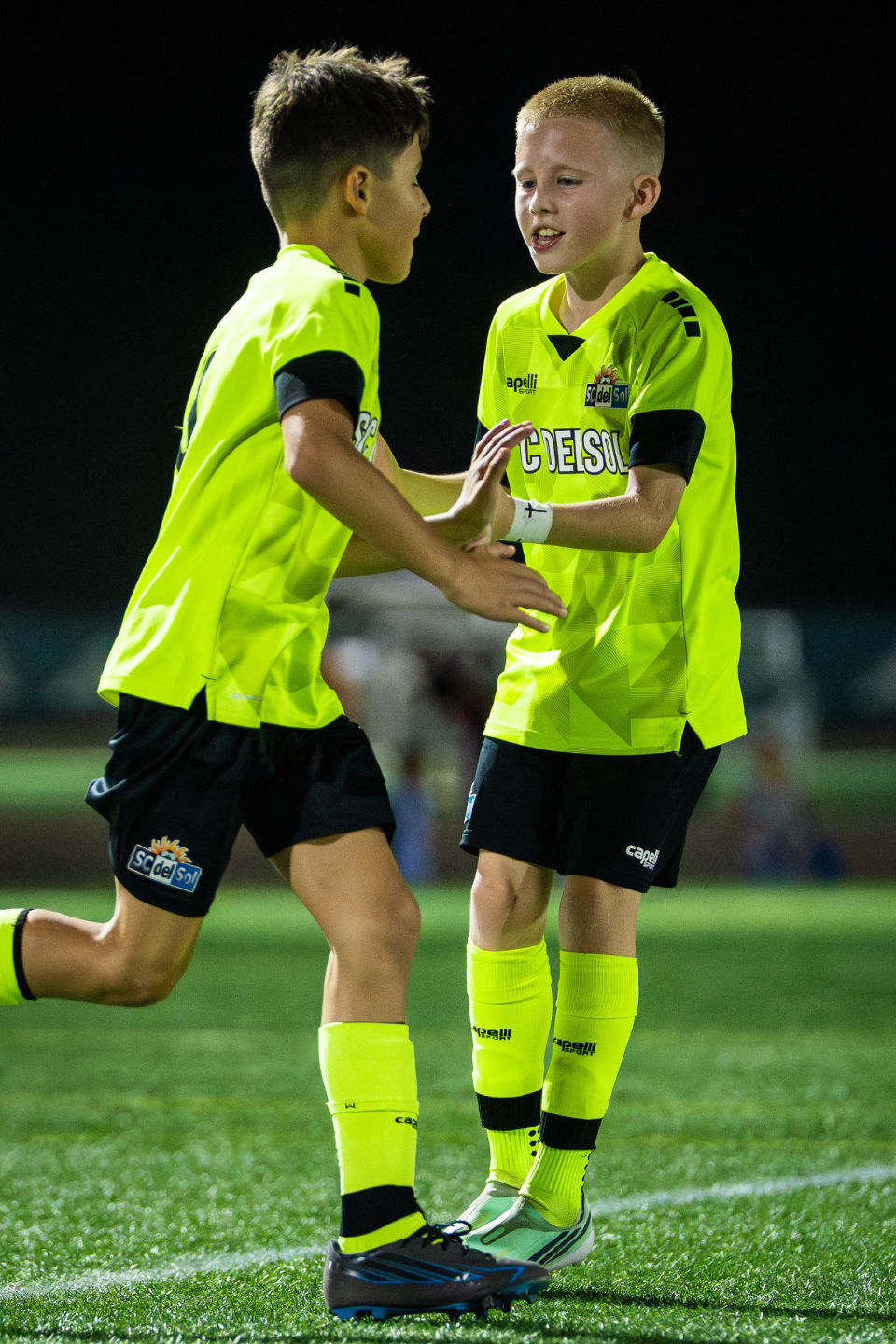 Two young soccer teammates celebrate together on the field.