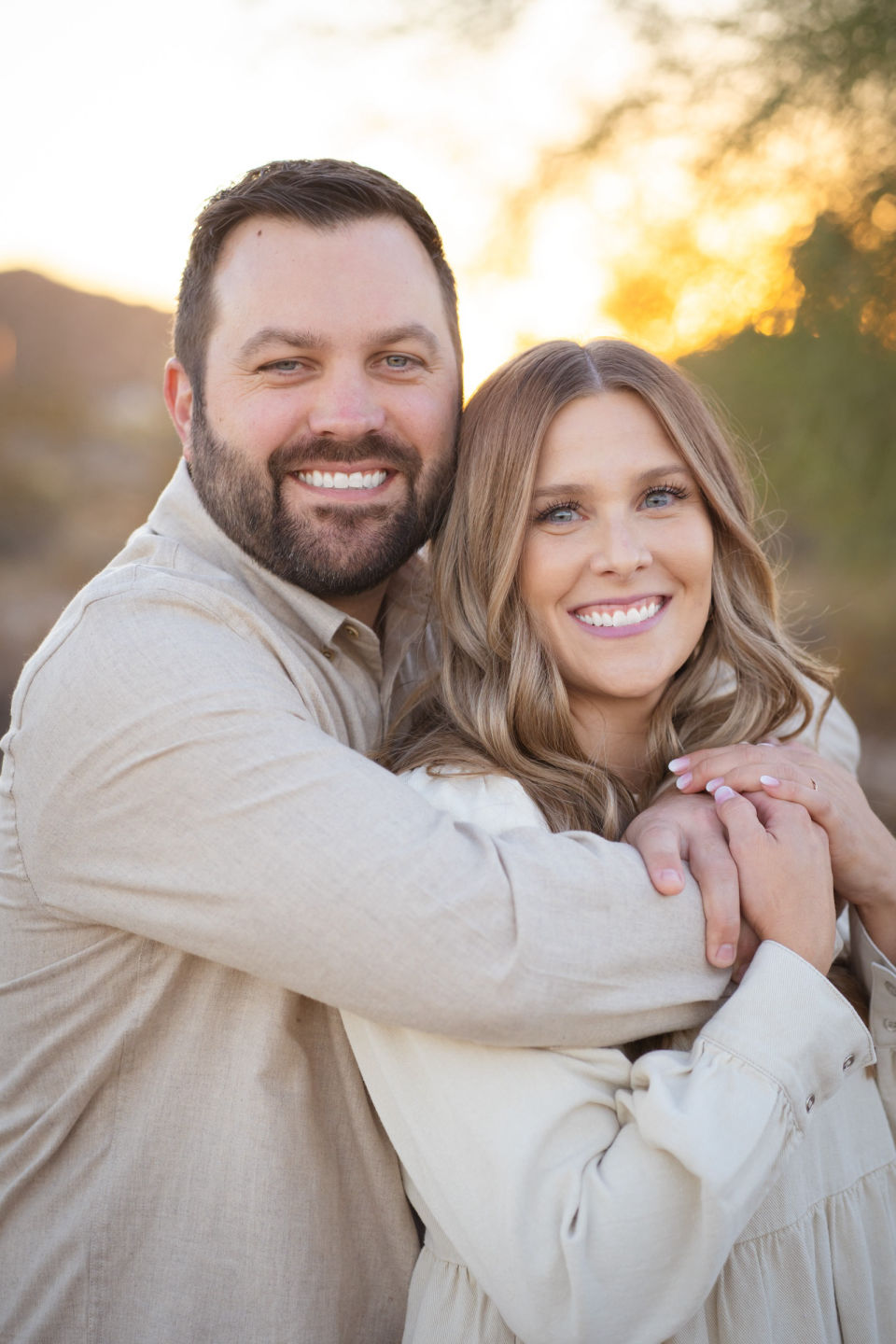 Parents embrace and smile in a close outdoor portrait.