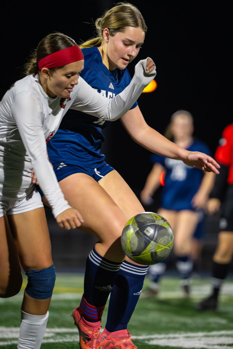 Two soccer players compete closely for an airborne ball under stadium lights.