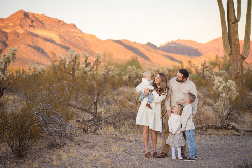 Family gathered together in the Arizona desert beneath sunlit mountains and a saguaro.