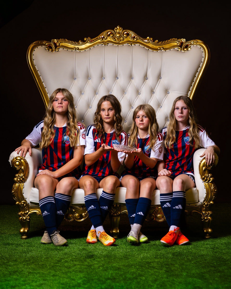 Four smiling soccer teammates sit together on the white-and-gold throne.