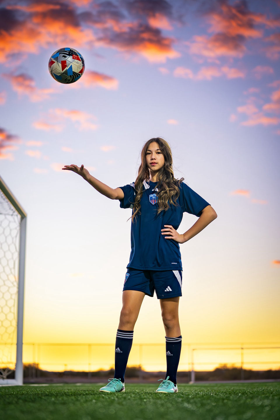 Soccer player tosses a ball beneath pink clouds above the turf field.