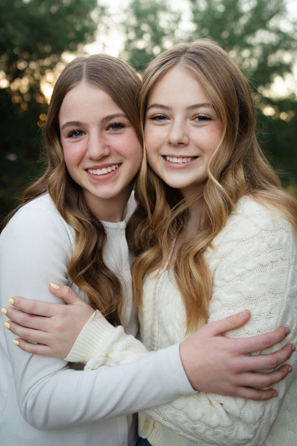 Two sisters embrace and smile outdoors.