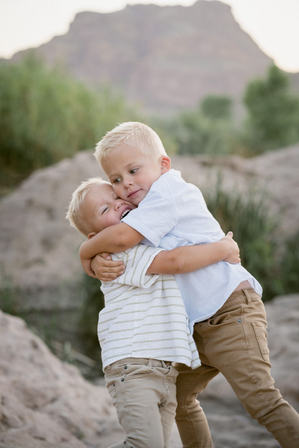 Two brothers share a playful hug against a mountain backdrop.