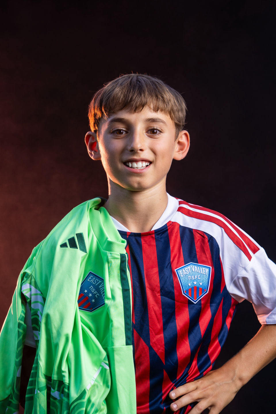 Smiling soccer player with a green goalkeeper jersey draped over his shoulder.