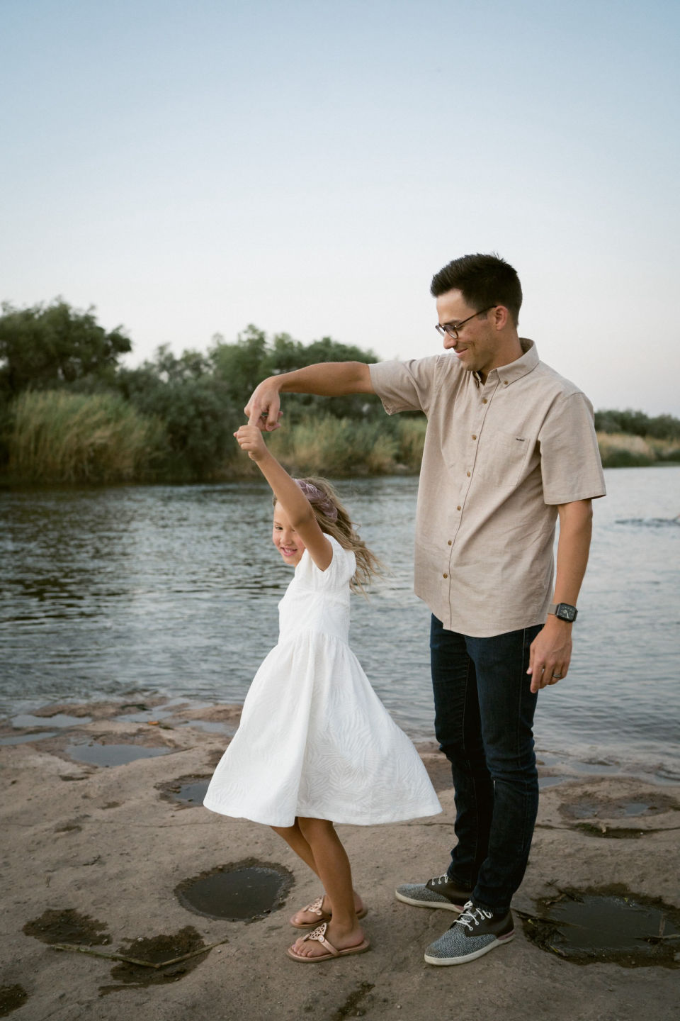 Father twirls his daughter beside the river.