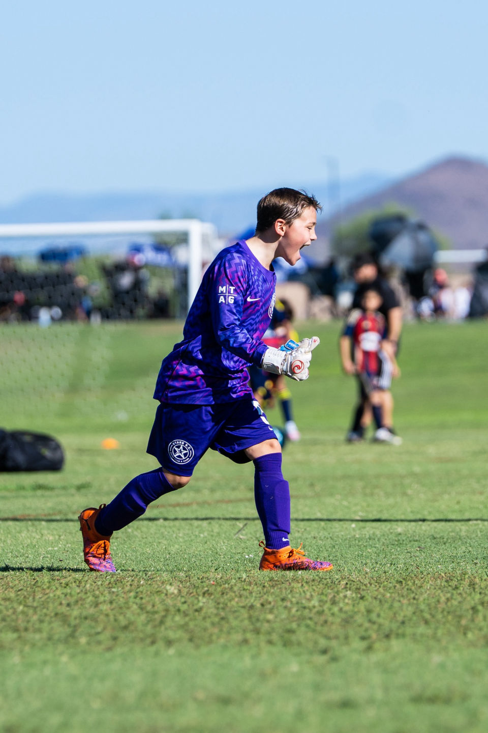 Goalkeeper in purple calls out to teammates while moving across the field.