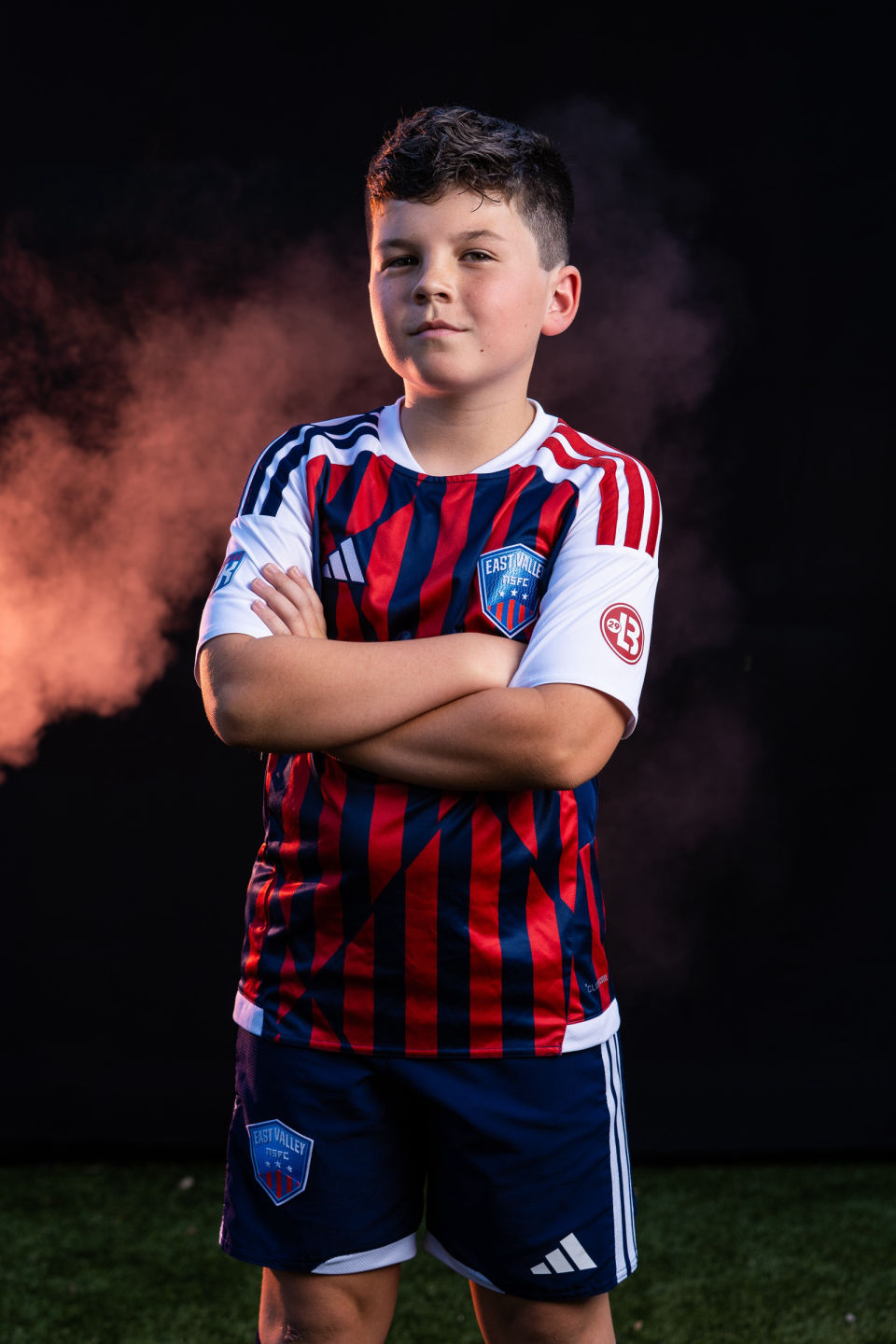 Soccer player poses with folded arms against orange smoke.