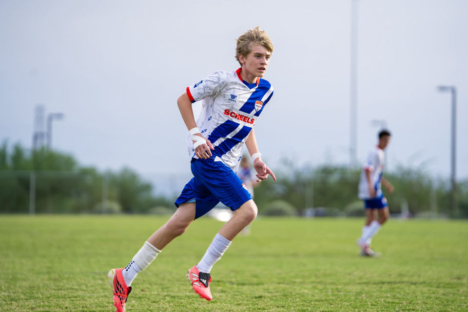 Soccer player in white and blue sprints across the field during a match.