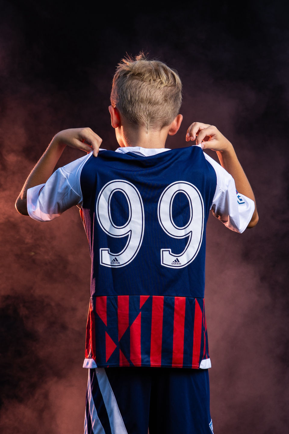 Soccer player shows the number 99 on his jersey against orange smoke.