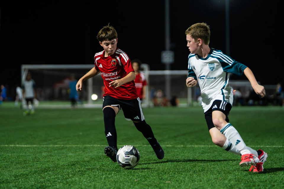 Players in red and white compete for the ball during a night soccer match.