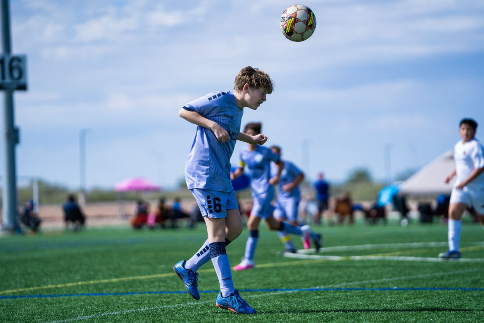 Soccer player in light blue prepares to control an airborne ball.