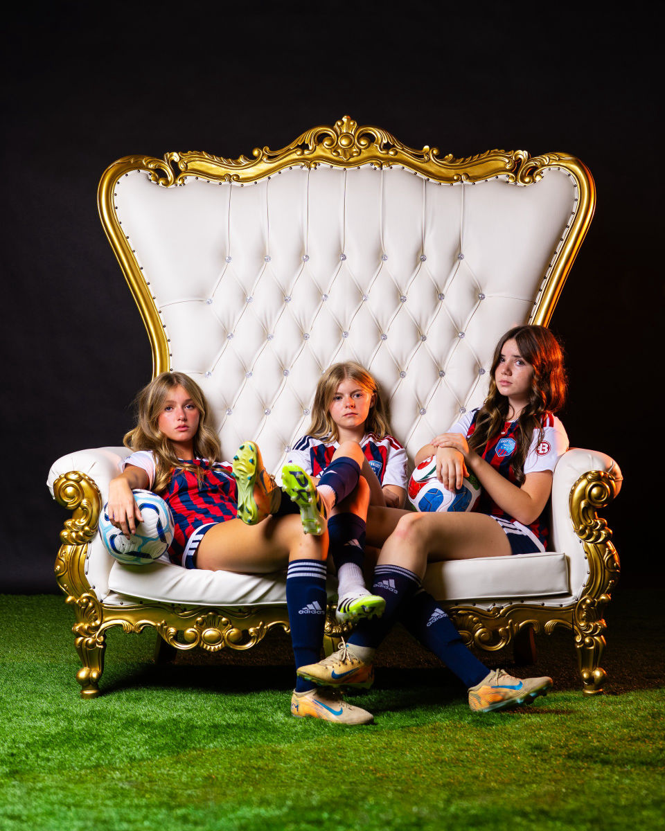 Three teammates lounge on a white and gold throne with soccer balls.