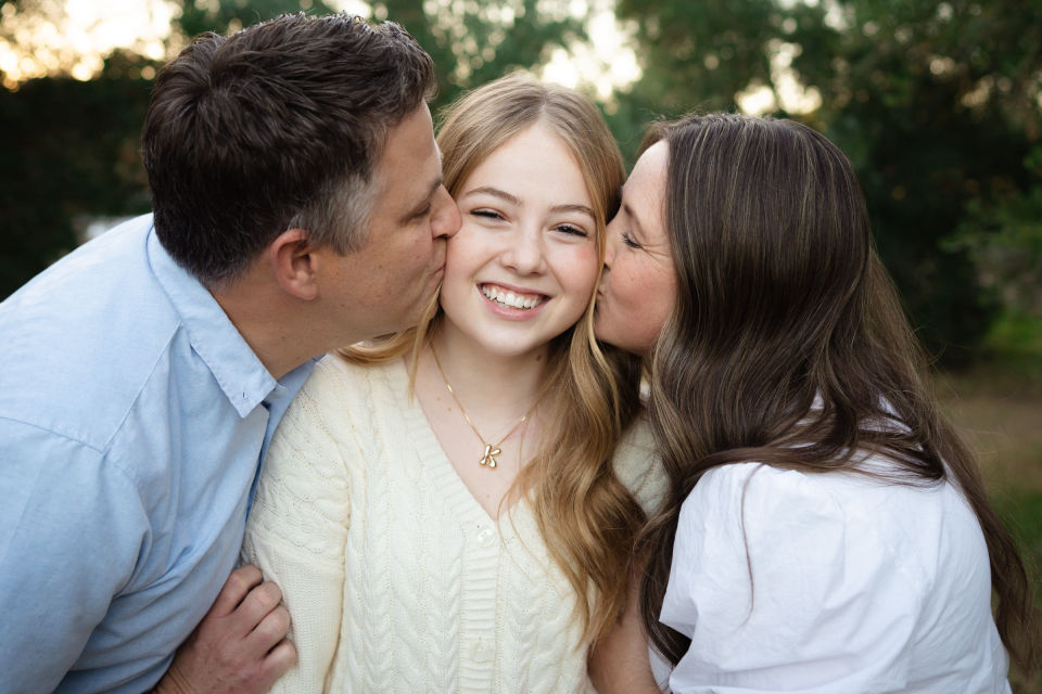 Parents kiss their smiling daughter on the cheeks.